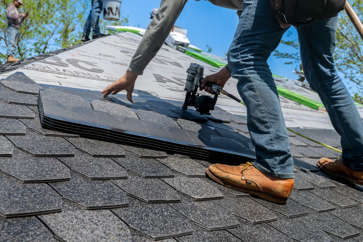 Roofer fitting new shingles during a full roof installation