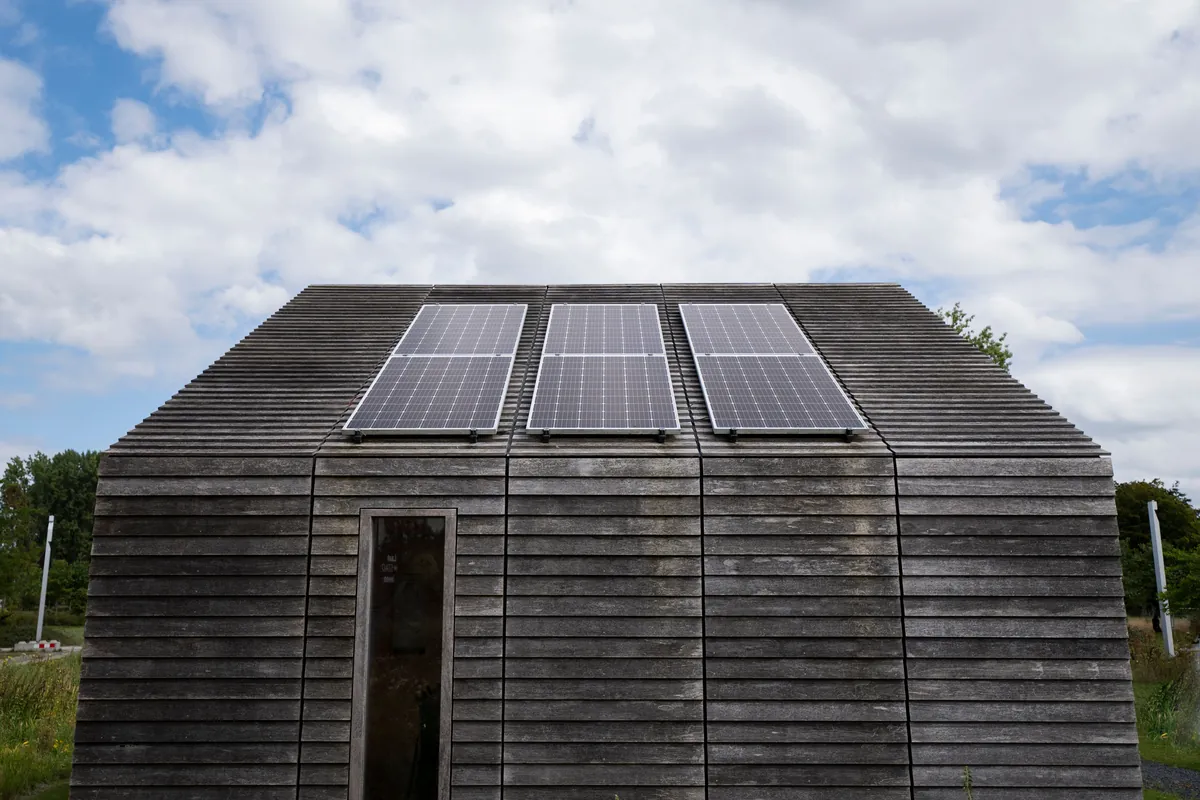 Dark timber-clad building with solar panels under an overcast sky